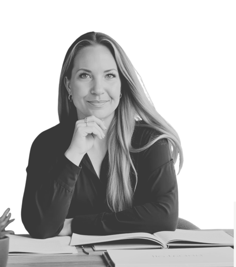 Foto Daniela Blöcker Ein Foto von Daniela Blöcker am Schreibtisch sitzend. Vor ihr Bücher aufgeschlagen auf dem Tisch. Sie schaut selbstbewusst in die Kamera.